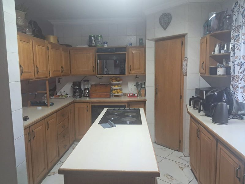 A functional kitchen featuring wooden cabinetry, a central island with a built-in electric hob, and tiled flooring throughout.