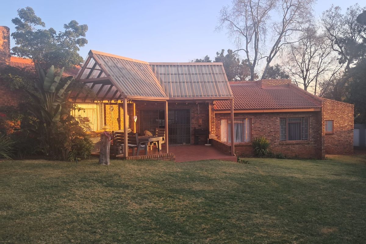 Rear view of a brick house featuring a covered patio area with translucent roofing and a spacious garden lawn.
