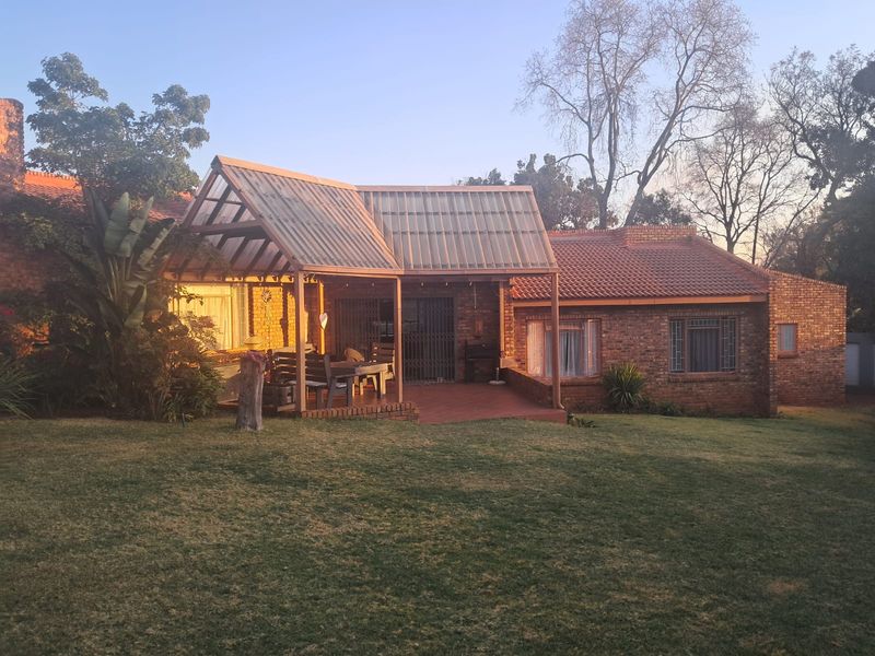 Rear view of a brick house featuring a covered patio area with translucent roofing and a spacious garden lawn.