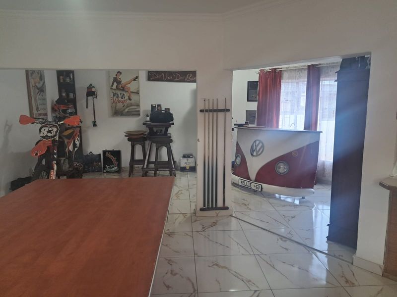 A spacious entertainment area featuring polished marble-look floor tiles and an open-plan layout, currently utilized as a home bar and recreational space.