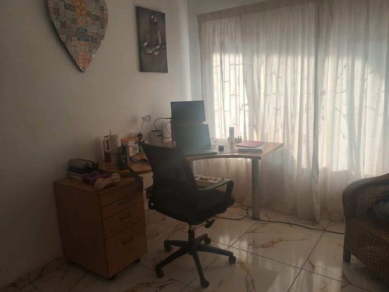 A functional home office space featuring tiled flooring and natural light through window curtains.