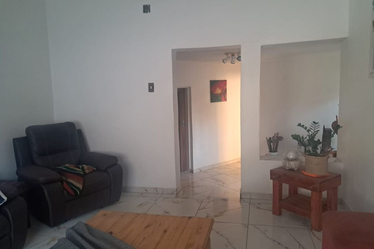 A living room featuring white walls, marble-look tiled flooring, and a built-in wall niche, leading into a connecting hallway.
