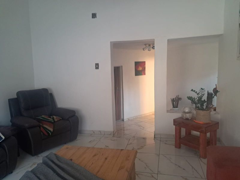 A living room featuring white walls, marble-look tiled flooring, and a built-in wall niche, leading into a connecting hallway.