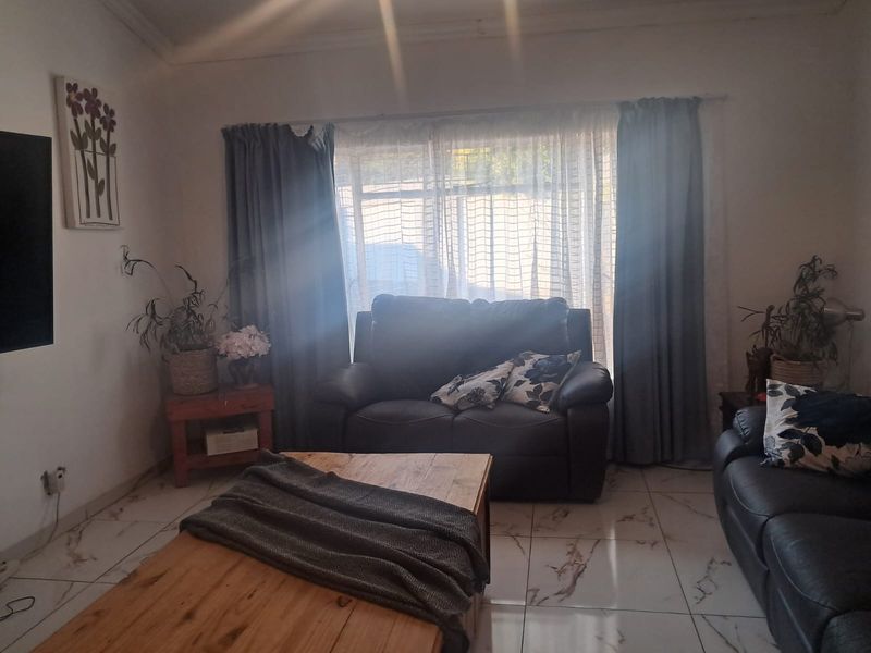 A living room featuring tiled flooring and large windows with curtain treatments, providing a bright and functional space.