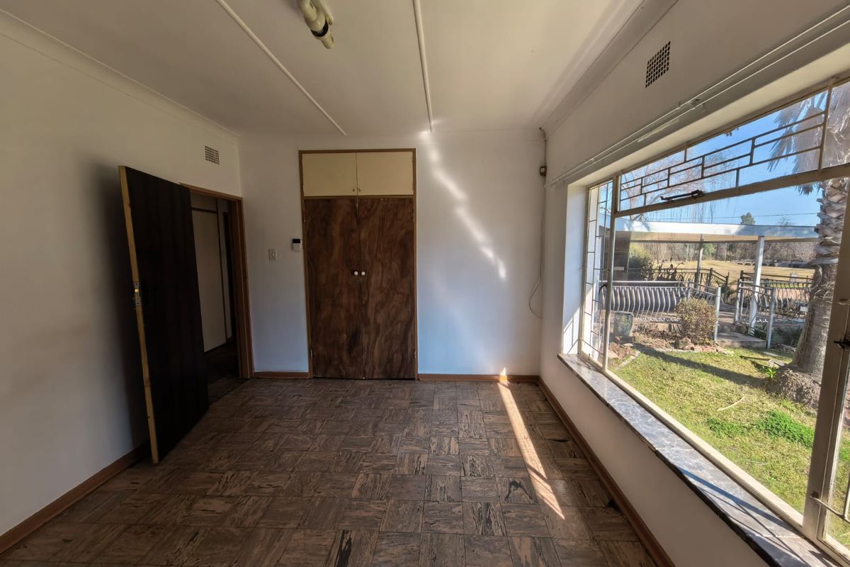An empty bedroom featuring original parquet flooring, built-in cupboards, and a large window overlooking the garden.