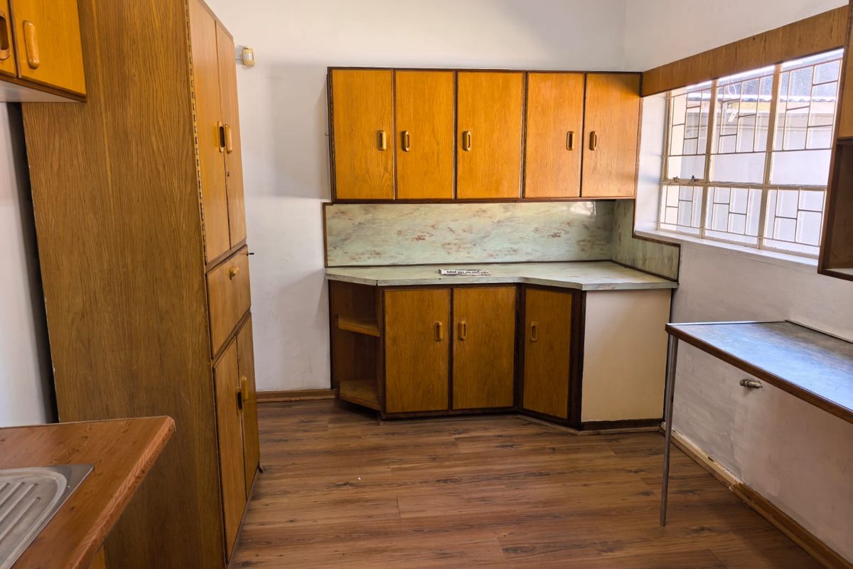A dated kitchen featuring original wood-look laminate cabinetry, laminate countertops, and wood-look flooring, offering a blank canvas for a modern renovation.