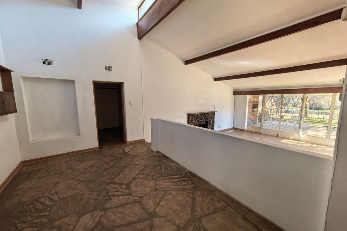 Spacious living area featuring vaulted ceilings with exposed timber beams, a stone fireplace, and unique flagstone flooring, offering a bright and open layout.