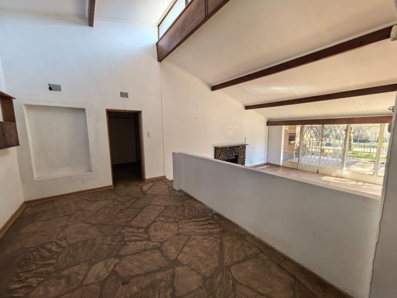Spacious living area featuring vaulted ceilings with exposed timber beams, a stone fireplace, and unique flagstone flooring, offering a bright and open layout.