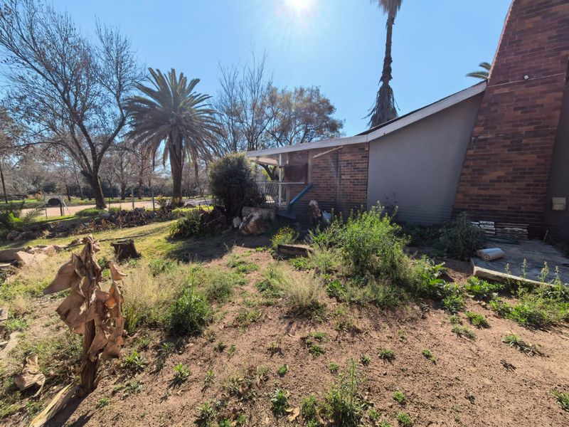 Rear view of the property featuring a brick chimney, covered patio area, and an expansive, unmaintained garden space.