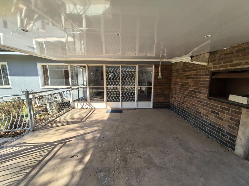 Covered outdoor patio featuring a built-in braai, concrete flooring, and metal security gates, offering a functional space for outdoor entertaining.