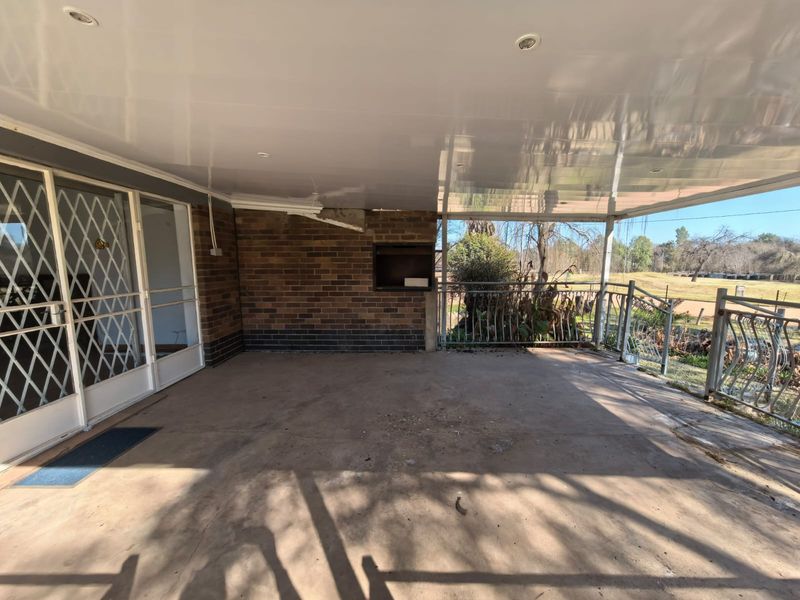 Covered outdoor patio featuring a built-in braai, metal security gate, and metal railing, offering a functional space for outdoor entertaining.