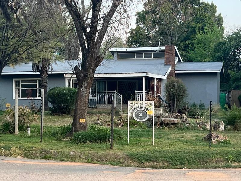 Front view of a single-story residential property featuring a metal roof, brick chimney, and a covered porch area set within a large garden.