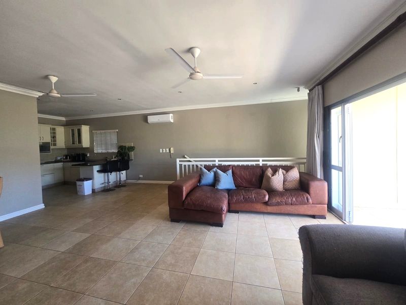 Spacious open-plan living area featuring tiled floors, ceiling fans, air conditioning, and a functional kitchen with an island, leading to a balcony.