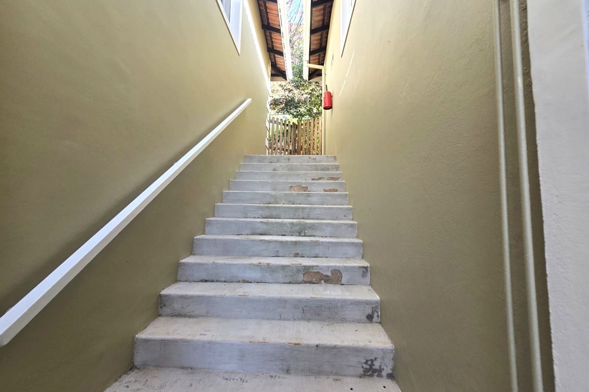 An exterior concrete staircase leading to a rear garden area, featuring a handrail and a fire extinguisher mounted on the wall.