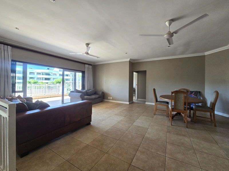 Spacious open-plan living and dining area featuring neutral tiled flooring, dual ceiling fans, and large sliding doors leading to an outdoor balcony.