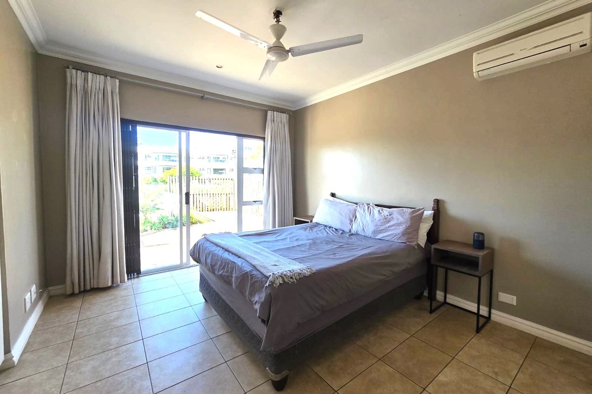 A bedroom featuring tiled flooring, a ceiling fan, and a wall-mounted air conditioning unit, with direct access to an outdoor area via sliding glass doors.