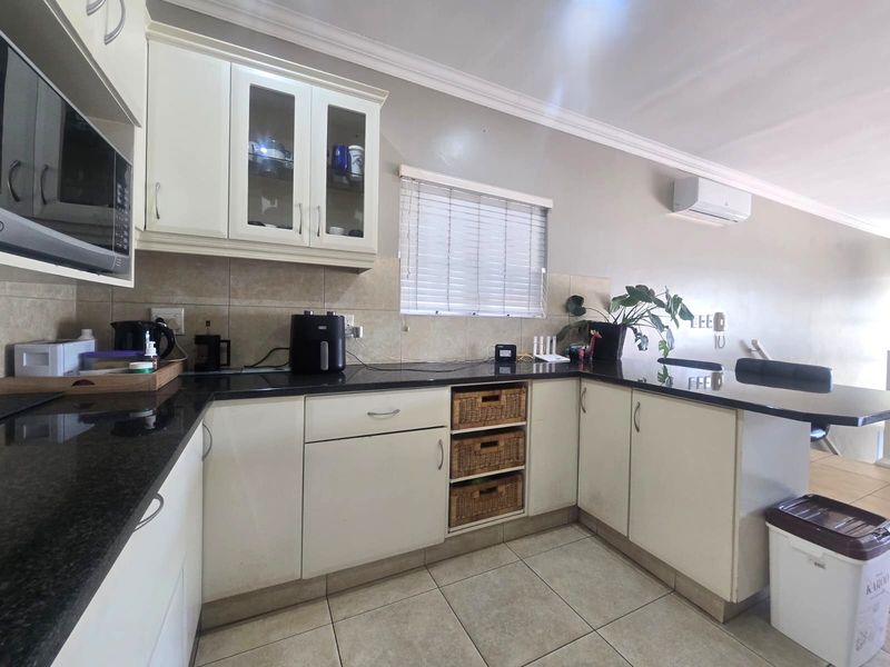 A functional kitchen featuring white cabinetry, dark granite countertops, tiled backsplash, and a built-in microwave, with an integrated breakfast bar area.