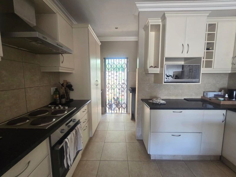 A functional kitchen featuring cream cabinetry, granite countertops, built-in appliances, and tiled flooring, leading to an exterior security gate.