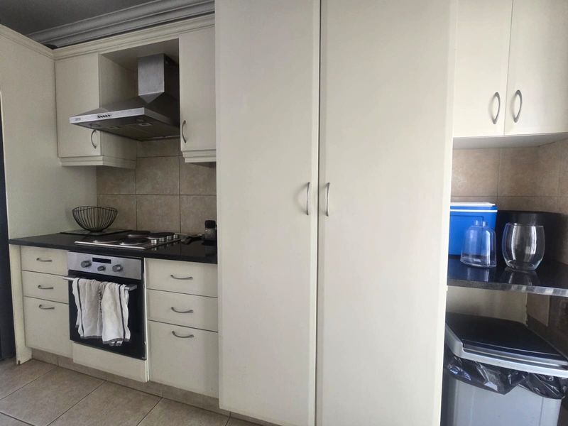 A functional kitchen featuring white built-in cabinetry, dark granite countertops, a stainless steel extractor fan, and a built-in oven with an electric hob.