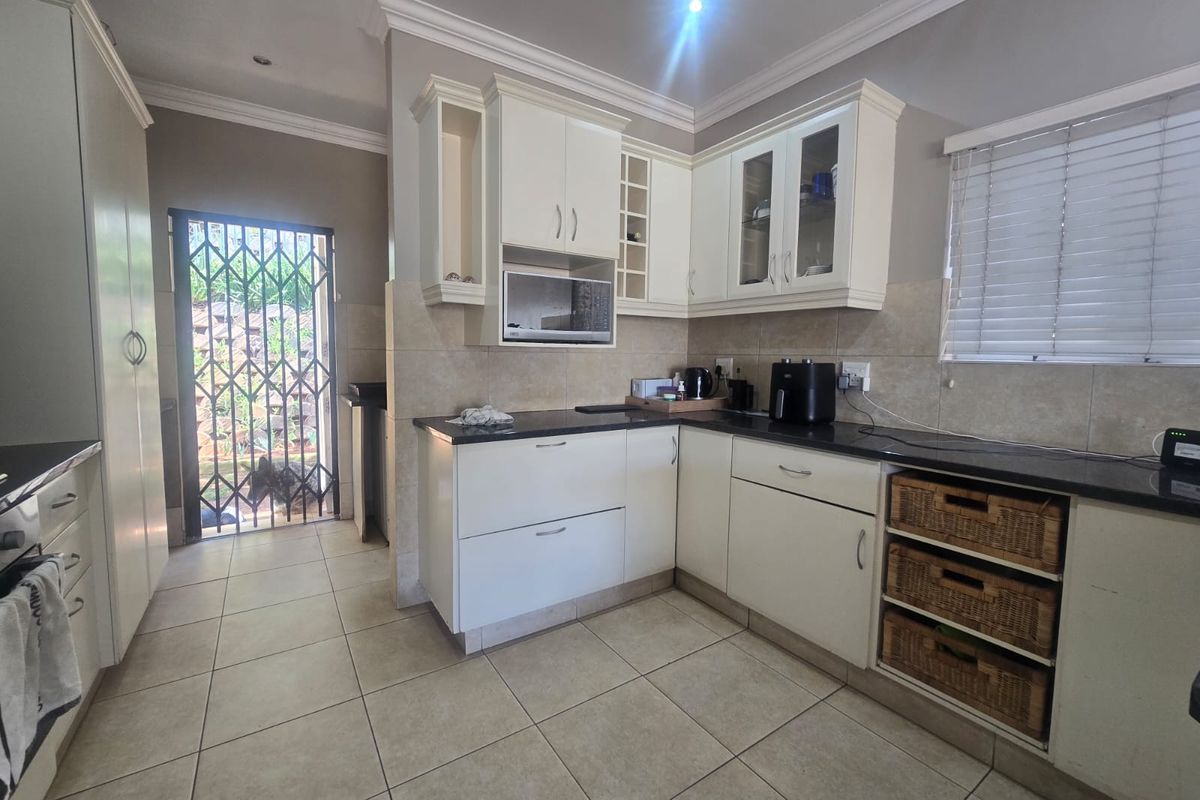 A functional kitchen featuring white built-in cabinetry, dark granite countertops, tiled flooring, and direct access to an outdoor area via a security gate.