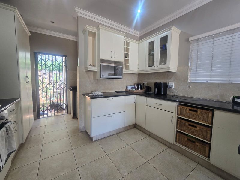 A functional kitchen featuring white built-in cabinetry, dark granite countertops, tiled flooring, and direct access to an outdoor area via a security gate.