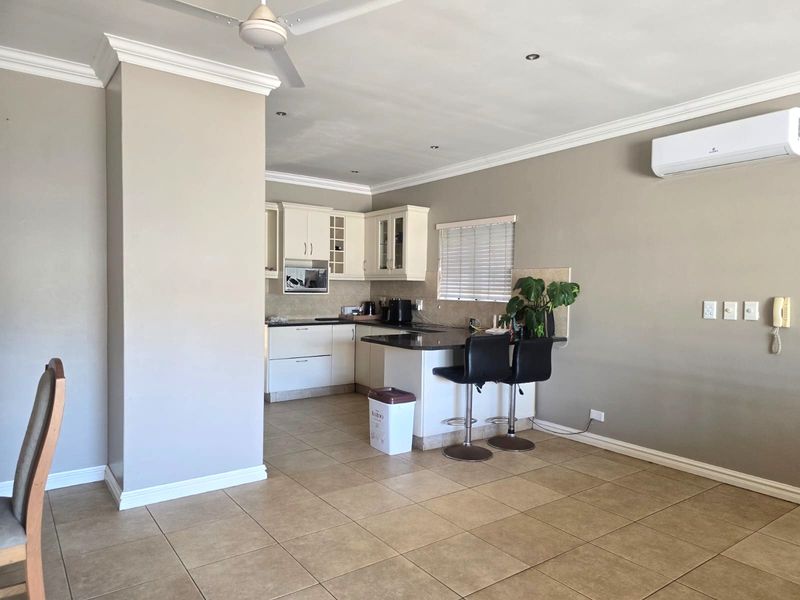 Open-plan living and kitchen area featuring tiled flooring, built-in cabinetry with granite countertops, a ceiling fan, and a wall-mounted air conditioning unit.