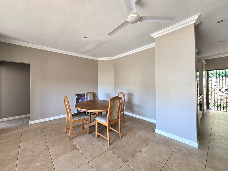 Open plan living and dining area featuring neutral wall tones, tiled flooring, crown molding, and a ceiling fan, with access to an exterior security gate.