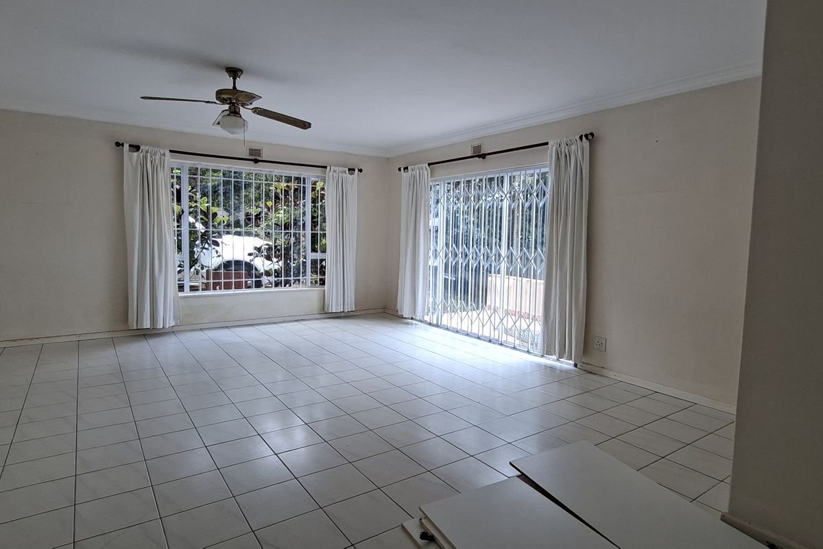 Spacious, empty living room featuring tiled flooring, a ceiling fan, and large windows with access to the exterior through a sliding glass door.