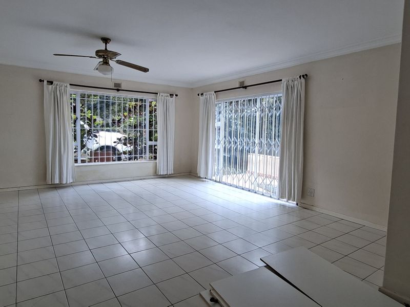Spacious, empty living room featuring tiled flooring, a ceiling fan, and large windows with access to the exterior through a sliding glass door.