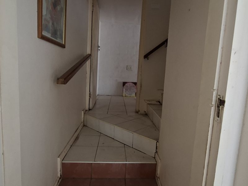 A narrow interior hallway featuring a tiled staircase with a wooden handrail, connecting different levels of the home.