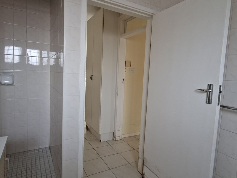 A functional bathroom featuring tiled walls and flooring, a shower enclosure, and built-in cabinetry, offering a blank canvas for renovation.
