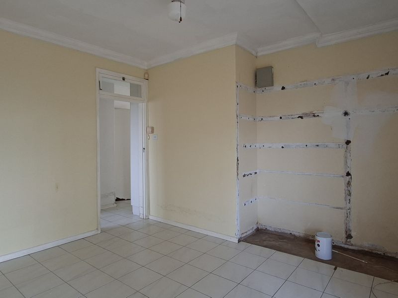 An empty living room featuring tiled flooring and coving, currently requiring wall repairs and cosmetic updates to restore the space.