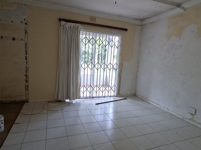 An empty living room featuring tiled flooring and a security gate, currently requiring wall repairs and cosmetic updates to restore its finish.