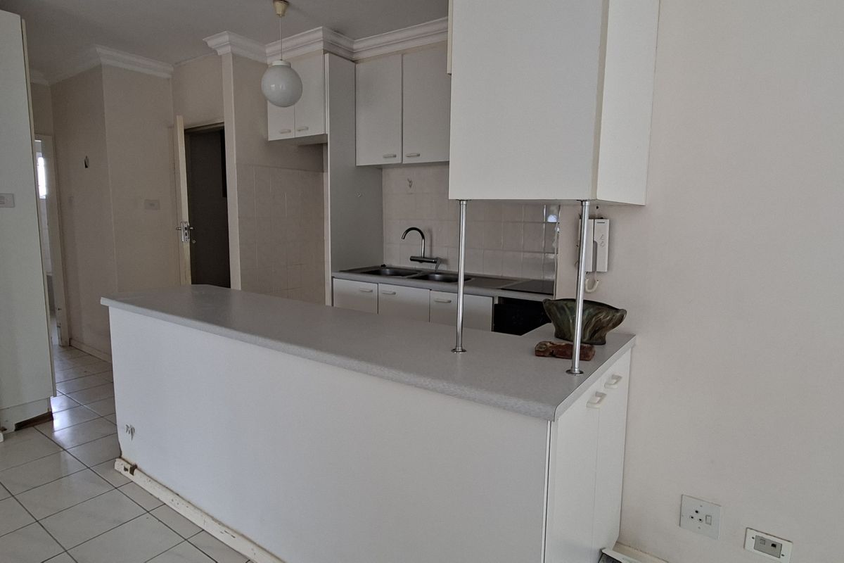A functional kitchen featuring white cabinetry, a breakfast bar, and tiled flooring, offering a clean canvas for potential modern updates.