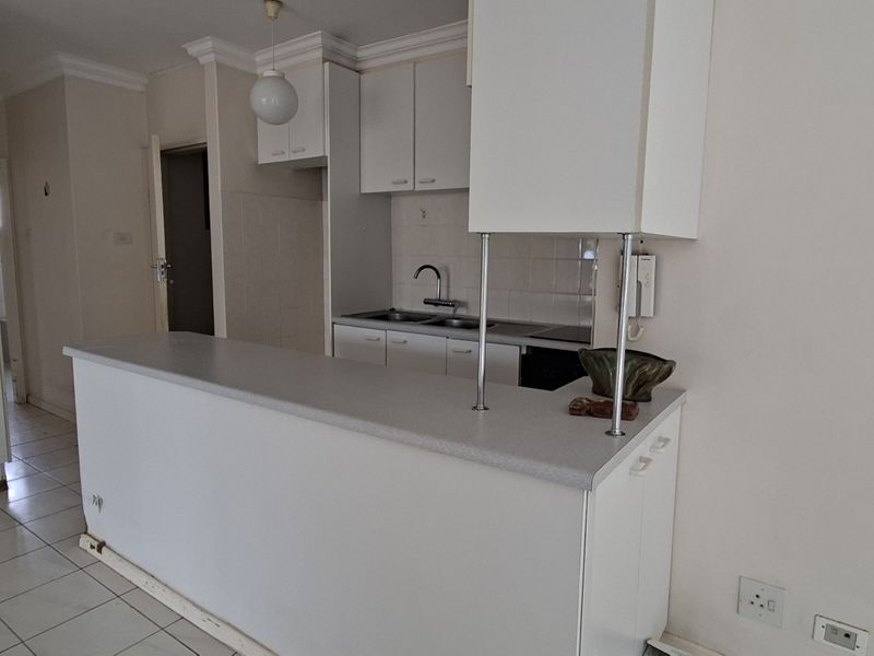 A functional kitchen featuring white cabinetry, a breakfast bar, and tiled flooring, offering a clean canvas for potential modern updates.