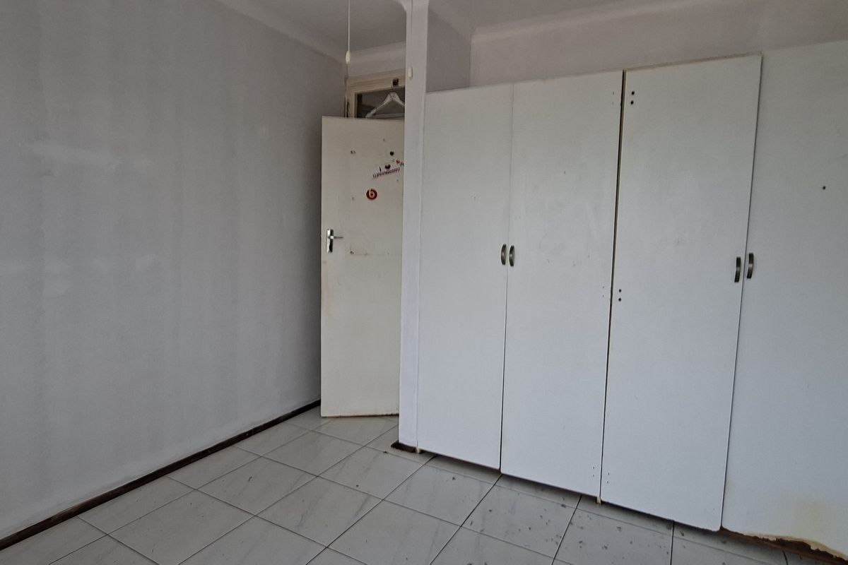 An empty bedroom featuring white built-in cupboards, tiled flooring, and a standard door. The space requires cosmetic updates and cleaning.