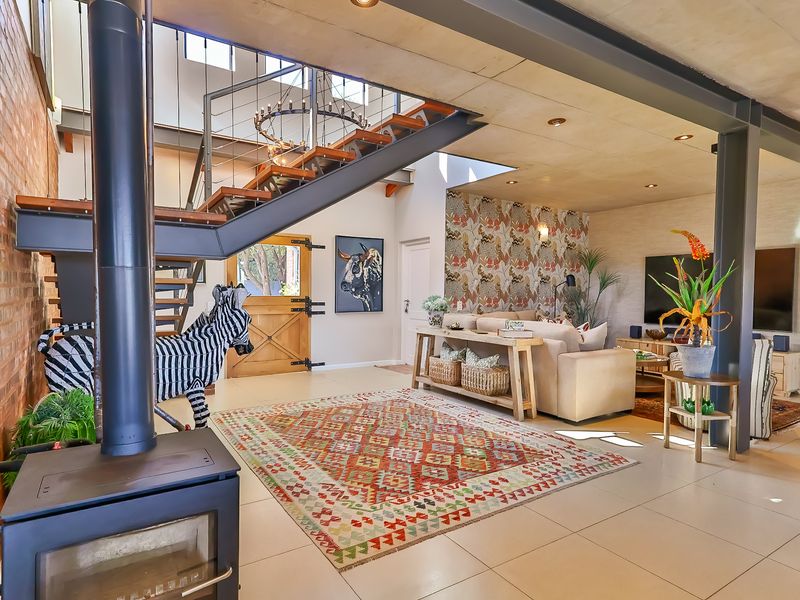 Spacious open-plan living area featuring exposed brickwork, industrial steel beams, a concrete ceiling, and a striking timber staircase with a modern fireplace.