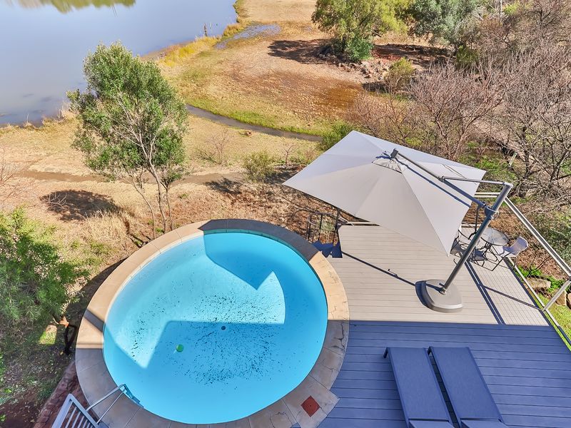 Elevated view of a circular swimming pool set into a timber deck, overlooking a natural landscape and water feature.