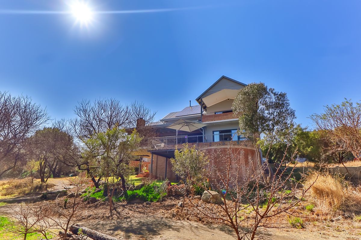 Rear view of a multi-level residential property featuring a brick facade, elevated balcony with glass balustrade, and roof-mounted solar panels.
