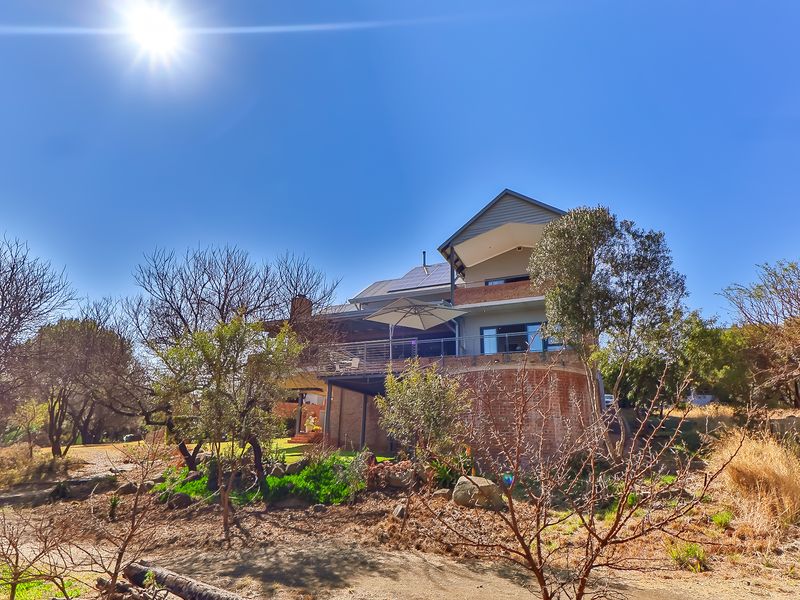 Rear view of a multi-level residential property featuring a brick facade, elevated balcony with glass balustrade, and roof-mounted solar panels.