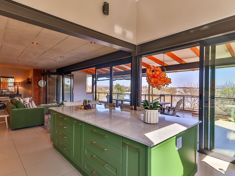 Modern open-plan kitchen and living area featuring a large island, stone countertops, and expansive sliding glass doors opening to a covered patio with views.