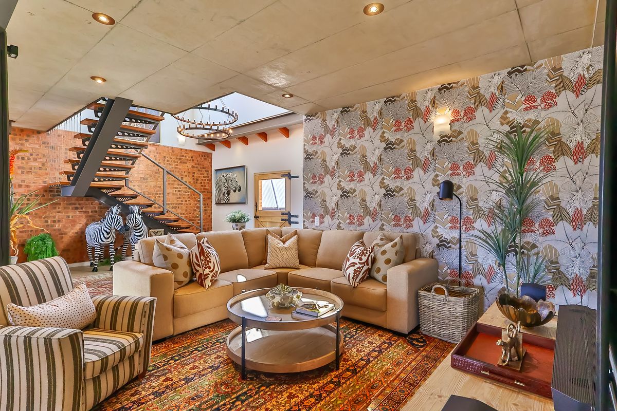 A stylish living room featuring an exposed concrete ceiling, a striking floating staircase, exposed brickwork, and a large skylight that fills the space with light.