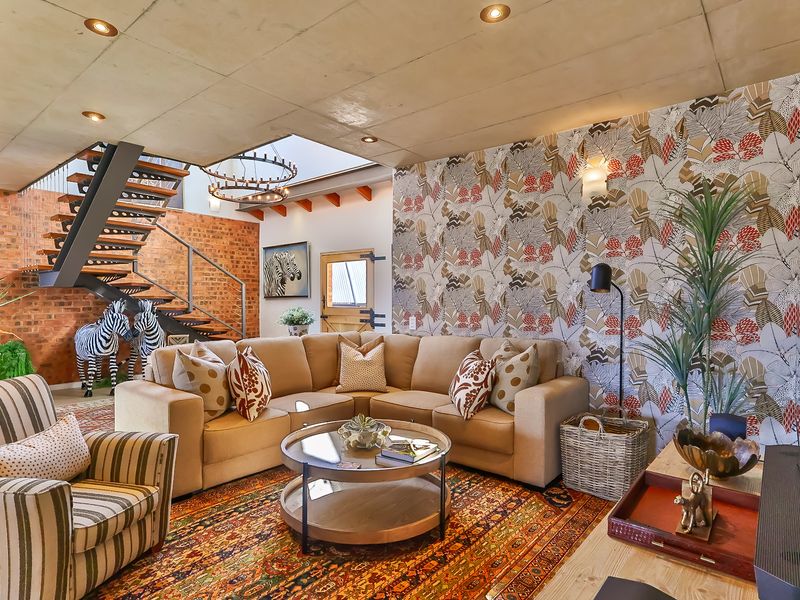 A stylish living room featuring an exposed concrete ceiling, a striking floating staircase, exposed brickwork, and a large skylight that fills the space with light.