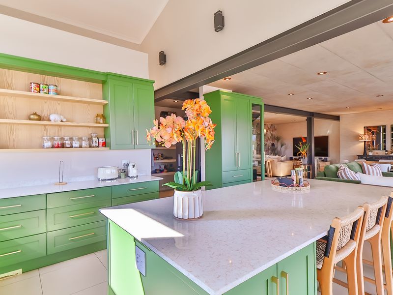 Modern open-plan kitchen featuring vibrant green cabinetry, a large central island with quartz countertops, and seamless flow into the adjacent living area.