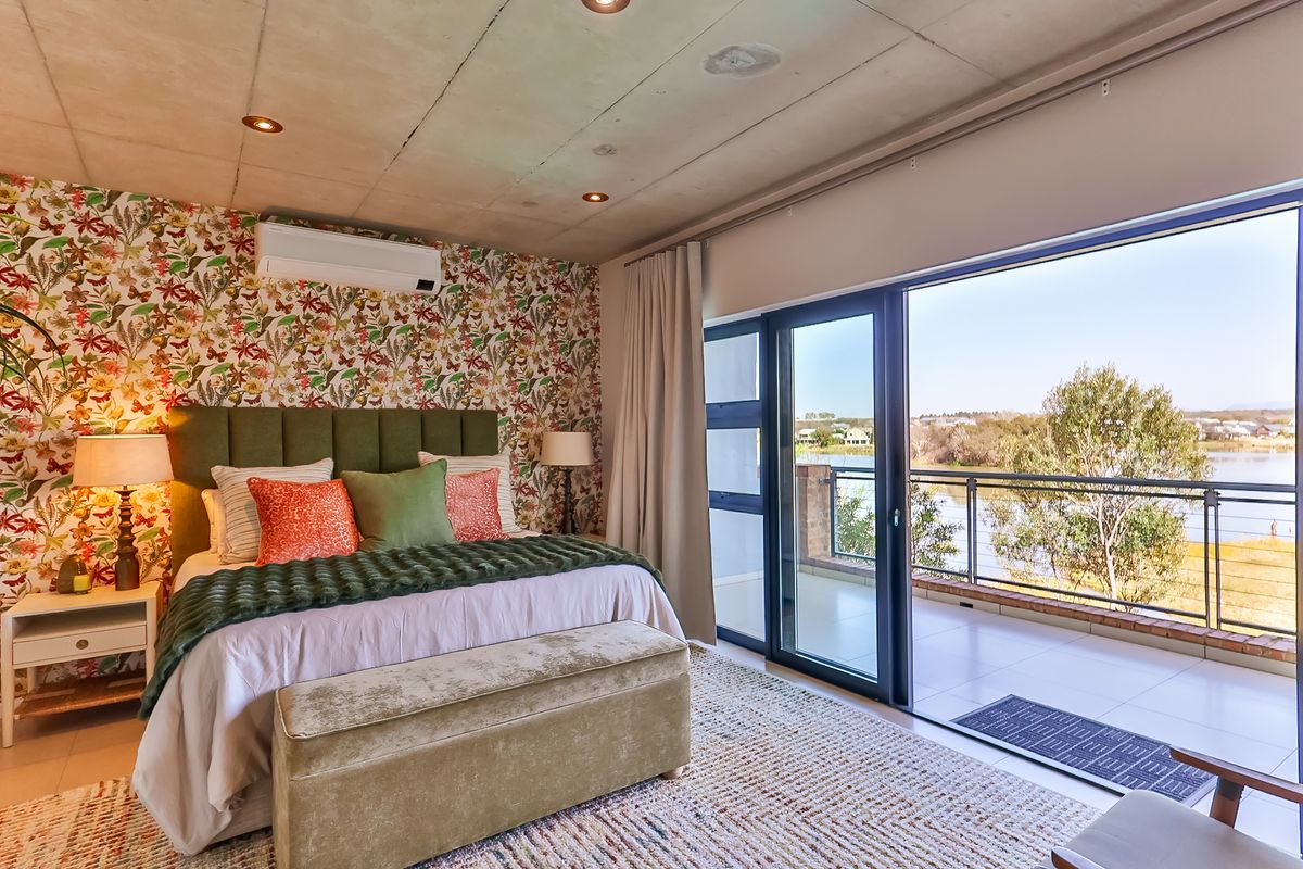 Spacious bedroom featuring an exposed concrete ceiling, split-system air conditioning, and large sliding glass doors opening onto a private balcony with scenic water views.