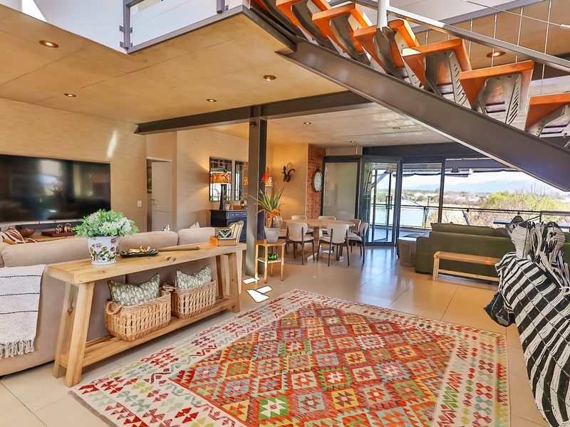 Spacious open-plan living and dining area featuring modern steel staircase, timber ceiling accents, and large sliding doors opening to an outdoor view.
