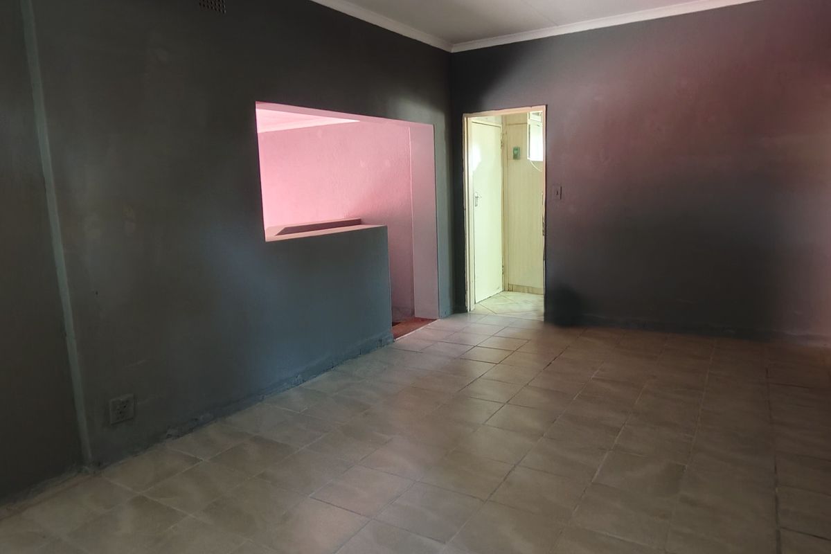 An empty living room featuring tiled flooring, coved ceilings, and a pass-through window connecting to an adjacent space.