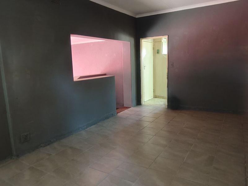An empty living room featuring tiled flooring, coved ceilings, and a pass-through window connecting to an adjacent space.