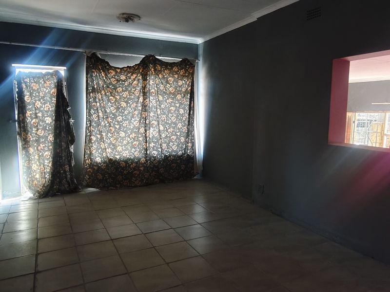 An empty living room featuring tiled flooring and a pass-through window connecting to an adjacent space, offering a blank canvas for renovation.