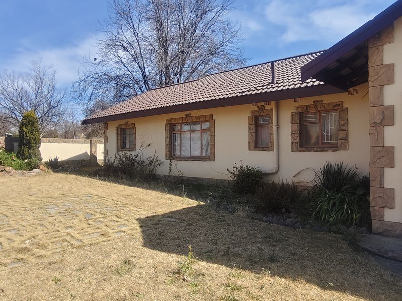 Rear exterior view of the house featuring a tiled roof, stone-clad window detailing, a security gate, and a paved patio area overlooking the garden.